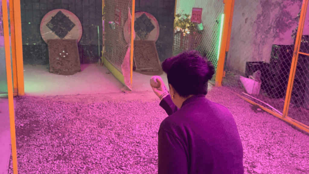 In the heart of Bogota's tourist attractions, a person readies themselves to throw an axe at a target in an indoor venue bathed in purple lighting.