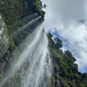 A tall waterfall cascading down a rocky, lush green cliff with a cloudy sky overhead is one of the many breathtaking sights you can explore during tours in Bogotá.