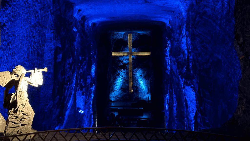 Discover a mesmerizing salt cave on our Day Tours from Bogota, where a large, illuminated cross is carved into the blue-lit underground chambers, and an angelic statue plays a trumpet in the foreground.