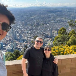 Three people capturing a selfie above the vibrant cityscape of Bogota, with lush greenery and bursts of yellow flowers in the foreground, perfectly capturing their day tour adventure.