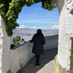 A person in a black coat strolls under an ivy-covered archway, taking in the vibrant cityscape during a sunny Bogota day tour.