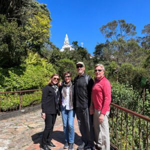 Four adults stand on a brick pathway, surrounded by lush greenery and a white tower in the backdrop under a clear blue sky, enjoying their Bogota day tour.