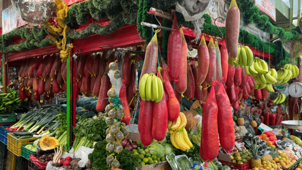 The vibrant Paloquemao Fruit Market stall showcases an enticing array of hanging cured meats, ripe bananas, and a colorful assortment of fresh fruits and vegetables.