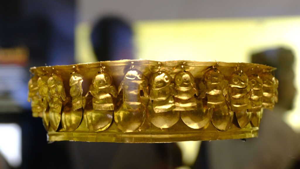 A golden, intricately designed ancient crown is on display in Bogota, featuring multiple sculpted figures around its band. This stunning piece makes for a must-see addition to any travel itinerary when exploring the city's rich history.