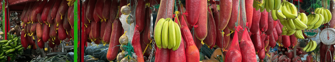 The vibrant Paloquemao Fruit Market stall showcases an enticing array of hanging cured meats, ripe bananas, and a colorful assortment of fresh fruits and vegetables.