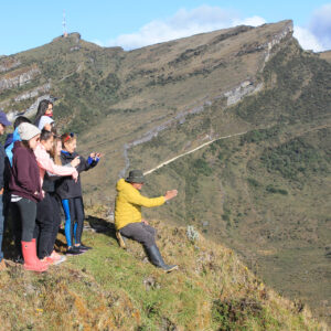 A group of people stands on a grassy hillside, some taking photos and pointing, enjoying one of the top things to do in Bogotá with a mountainous landscape in the background.