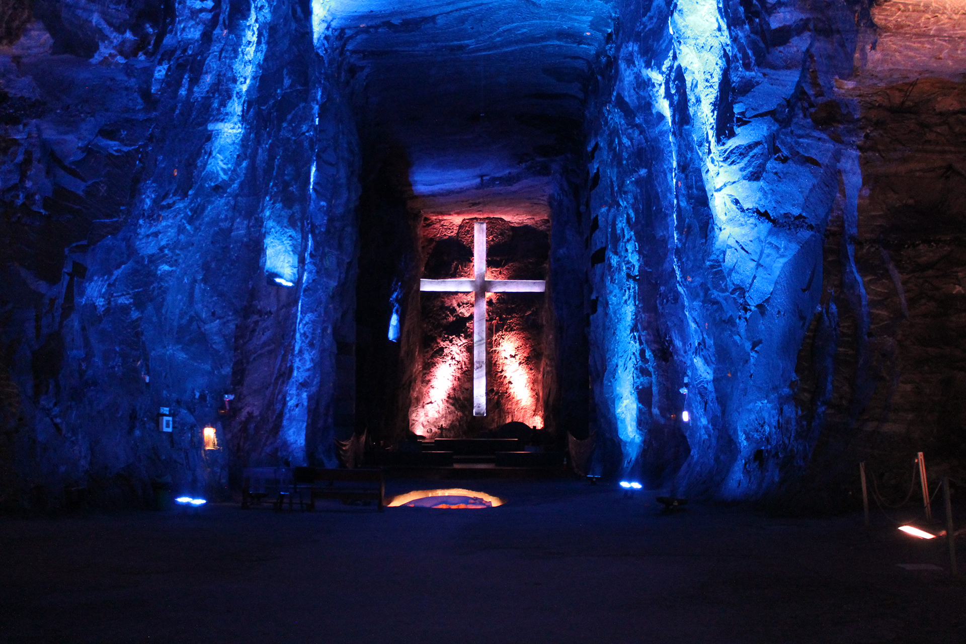 A large stone cross is illuminated in blue and white light against the backdrop of a cave with textured rock walls—a must-see when exploring tours in Bogotá.