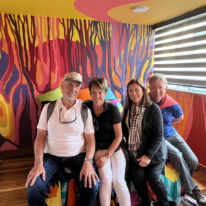 Four people pose together in front of a vibrant, abstract mural featuring colorful tree-like designs on a wall, a perfect snapshot from one of the many exciting Bogotá city tours.