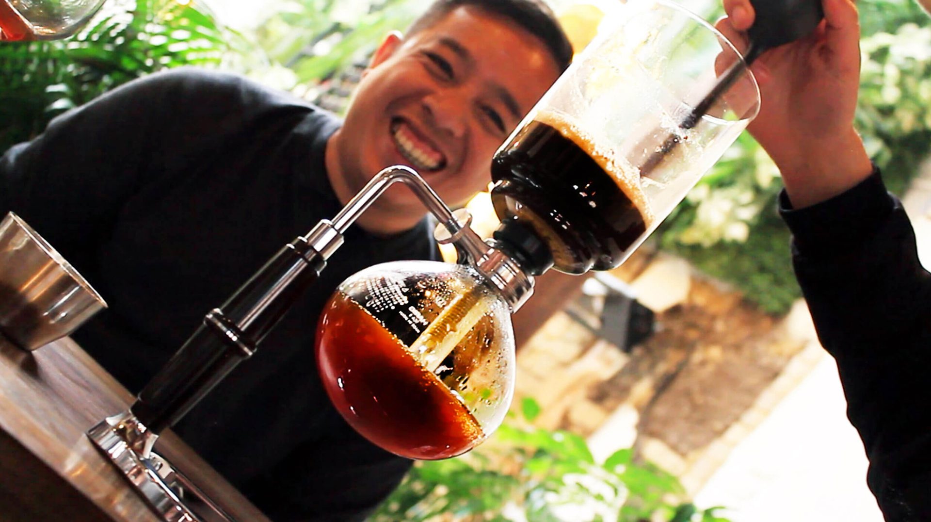 A person smiling while preparing coffee using a siphon coffee maker at a cafe, one of the unique things to do in Bogotá.