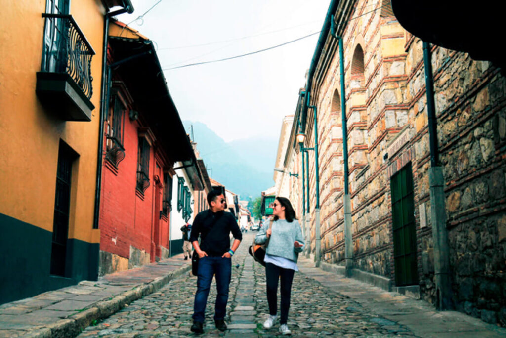 Two people walk down a cobblestone street lined with historic buildings, engaged in conversation. It’s one of the many enchanting sights you’ll encounter on Bogotá city tours.